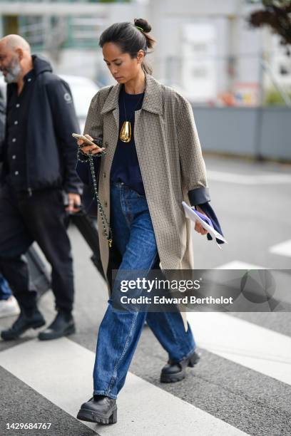 Guest wears a neon yellow hair elastic, a beige and black checkered print pattern long coat, a navy blue t-shirt, blue denim large pants, black shiny...