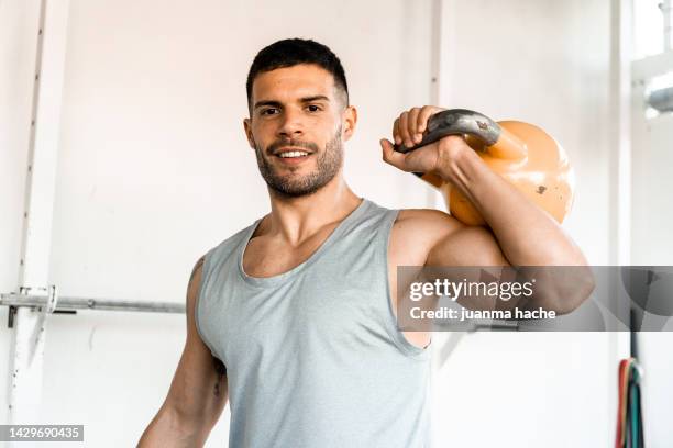 man smiling at the camera while holding kettlebell over his shoulder. - mann freundlich sport stock-fotos und bilder