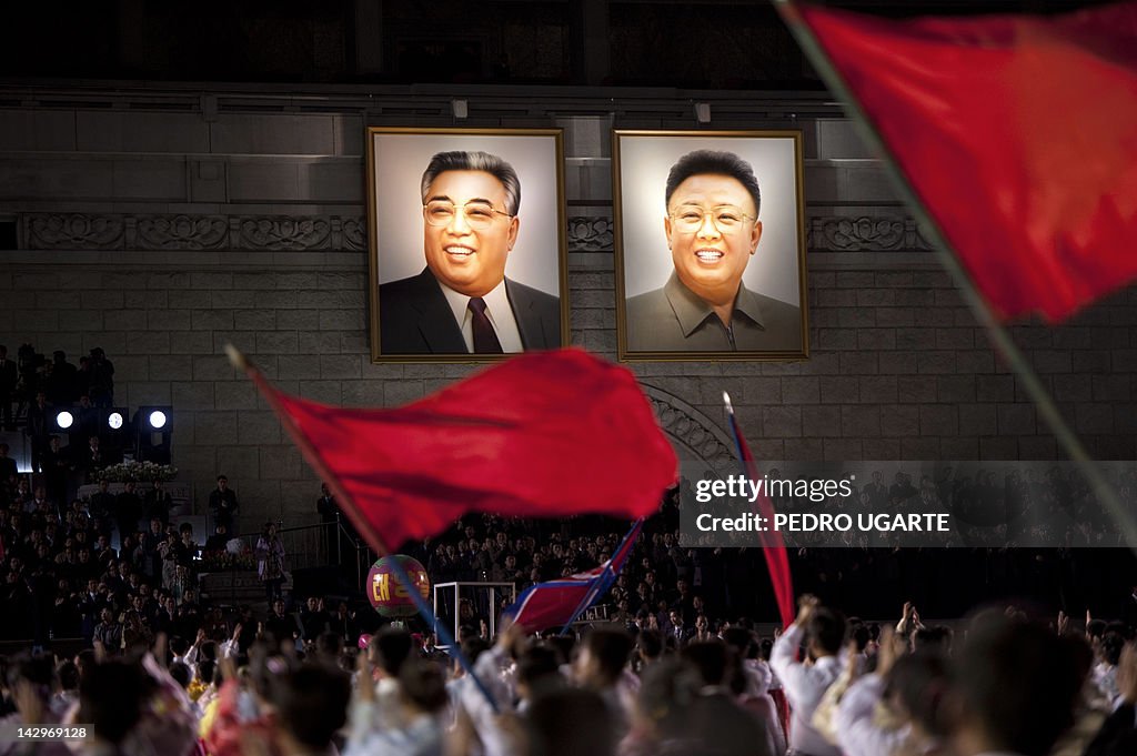 North Koreans wave flags in front of por