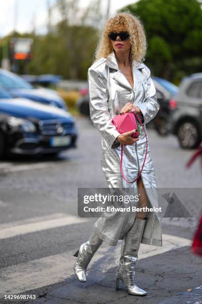 Guest wears black sunglasses, a silver shiny leather zipper long coat, a pale red shiny leather handbag, silver shiny leather crocodile print pattern...