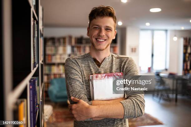 smiling student in library holding book looking at camera - choice student stockfoto's en -beelden