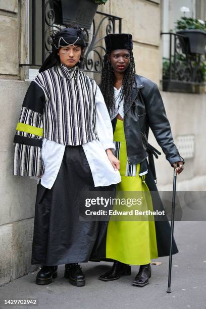Guest wears black with embroidered silver chains details hat, a black and white striped print pattern oversized jacket with a black and neon large...