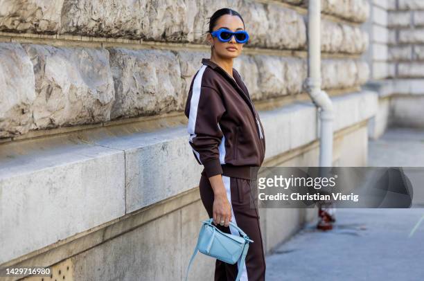 Amina Muaddi wears blue sunglasses, brown track suit with logo, turquoise bag outside Loewe during Paris Fashion Week - Womenswear Spring/Summer 2023...