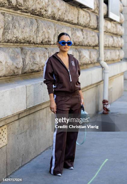 Amina Muaddi wears blue sunglasses, brown track suit with logo, turquoise bag outside Loewe during Paris Fashion Week - Womenswear Spring/Summer 2023...