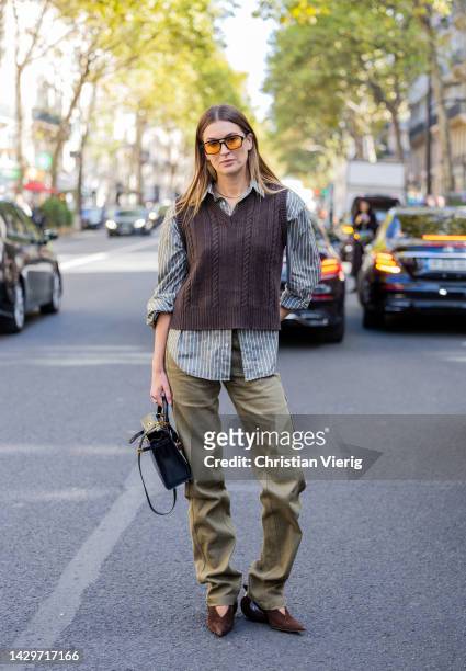Camille Charriere wears brown v neck pull under, striped button shirt, green pants, black Hermes bag, brown heels outside Loewe during Paris Fashion...