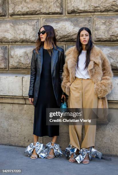 Giorgia Tordini wears black leather blazer, black dress, silver heels & Gilda Ambrosio wears beige faux fur coat, pants, silver heels with bow tie,...
