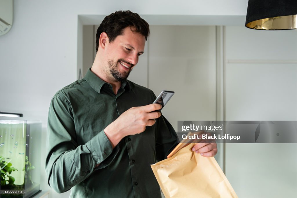 A man opening an envelope, holding smart phone, smiling.