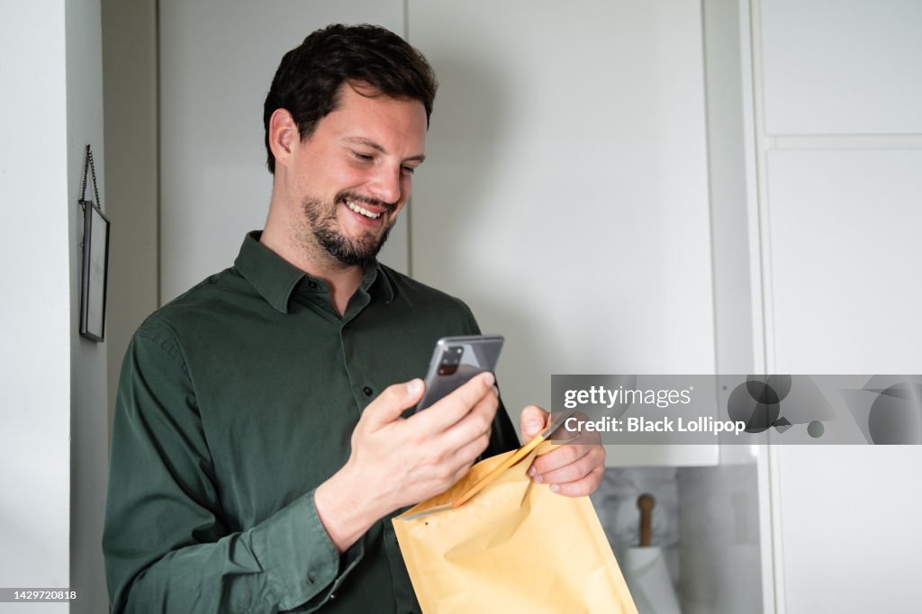 A man opening an envelope, holding smart phone, smiling.
