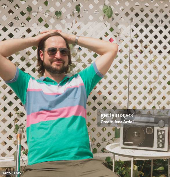 retro 1980s man relaxing, happy man wearing 1980s style fashion listening to music from vintage radio - backyard retro stock-fotos und bilder