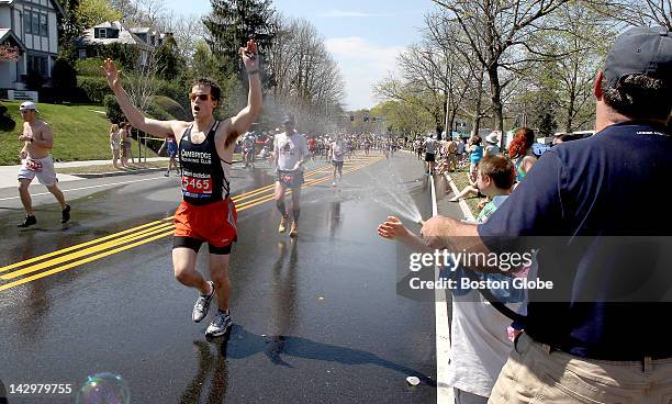 Joe Verdone, right, offers cooling relief with his garden hose for runners climbing Heartbreak Hill during the Boston Marathon on Commonwealth Avenue...