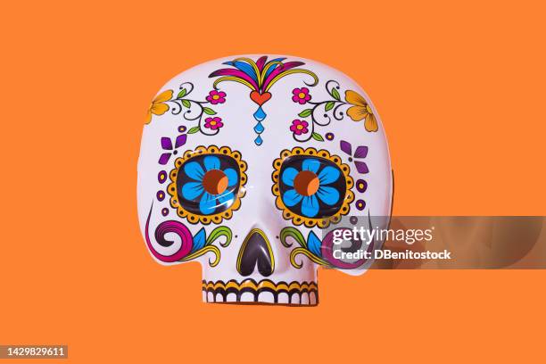 white and multicolored skull-shaped mask, from the day of the dead, typical of mexico, on a orange background. halloween, day of the dead, celebration, costume and spirits concept. - la catrina stockfoto's en -beelden