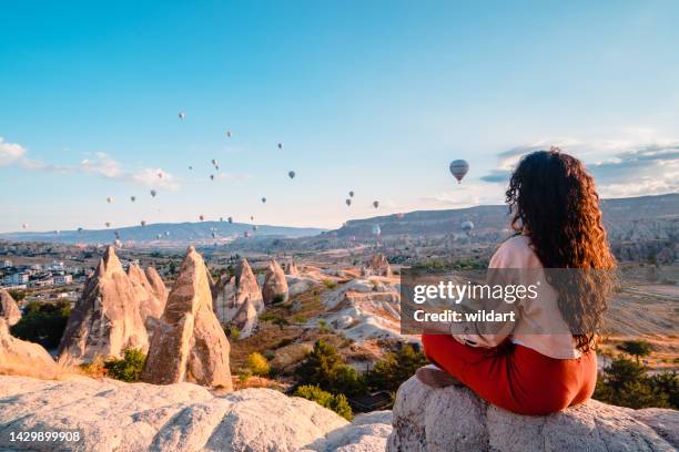 reisendes junges mädchen meditiert, macht yoga, während sie die heißluftballons während des sonnenaufgangs in kappadokien nevsehir, türkei beobachtet - göreme stock-fotos und bilder