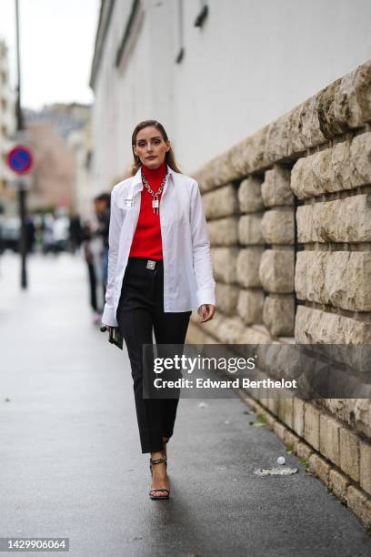 Olivia Palermo wears a silver large chain pendant necklace from Givenchy, a red ribbed wool turtleneck pullover, a white blazer jacket, a black shiny...