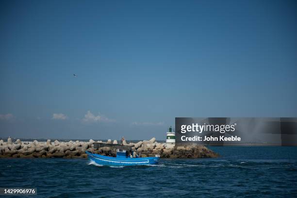 Blue fishing boat sails past Tavira Island Beach on the Gilão River on September 22, 2022 in Tavira, Portugal.