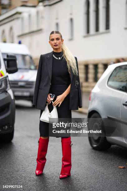 Xenia Adonts wears gold earrings, a black high neck midi dress, a silver large chain necklace from Givenchy, a black blazer jacket from Givenchy, a...