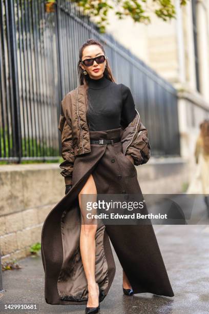 Chriselle Lim wears black sunglasses, silver earrings, a black ribbed wool turtleneck pullover, a brown nylon oversized nylon bomber coat, a dark...