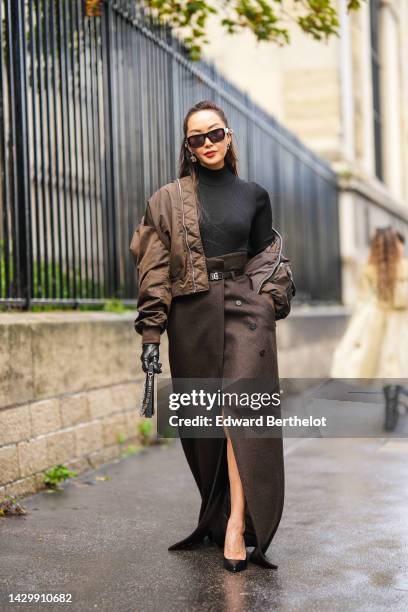 Chriselle Lim wears black sunglasses, silver earrings, a black ribbed wool turtleneck pullover, a brown nylon oversized nylon bomber coat, a dark...