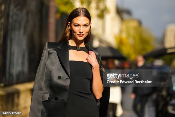 Karlie Kloss wears gold earrings, a black necklace / cut-out chest / tube short dress from Givenchy, a black satin blazer jacket, outside Givenchy,...
