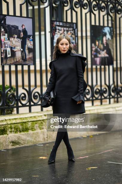 Jenny Tsang in Suet wears gold earrings, a black wavy high neck / long sleeves short dress, a black shiny leather clutch from Valentino, black...