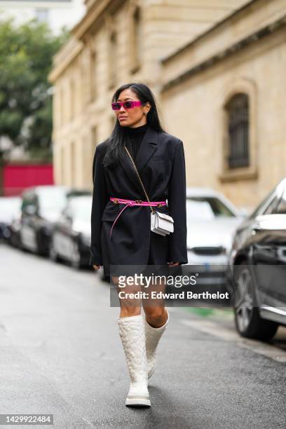 Miki Cheung wears gold earrings, neon pink square sunglasses, a black turtleneck pullover, a black oversized blazer jacket, a neon pink shiny leather...