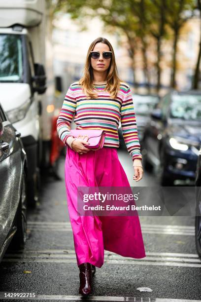 Maria Rosaria Rizzo wears beige sunglasses, a gold large chain necklace, a multicolored print pattern long sleeves pullover, a pale pink shiny...