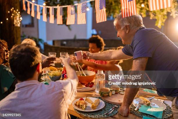 multi-generation family having dinner outdoors on an american national holiday - fourth of july party stock pictures, royalty-free photos & images