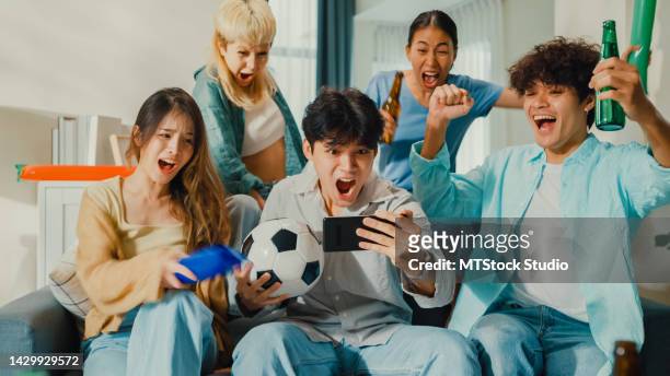 group of happy asian teenage people sit on couch watch cheering sport soccer games together on smartphone. - asian championship bildbanksfoton och bilder