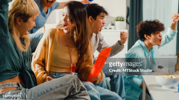 eine gruppe glücklicher asiatischer teenager sitzt auf der couch und schaut sich gemeinsam jubelnde sportfußballspiele an. - ball on a table stock-fotos und bilder