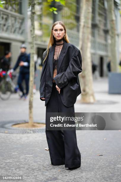 Pernille Teisbaek wears gold and diamonds earrings, a black tulle high neck / long sleeves blouse, a black oversized blazer jacket, black large suit...