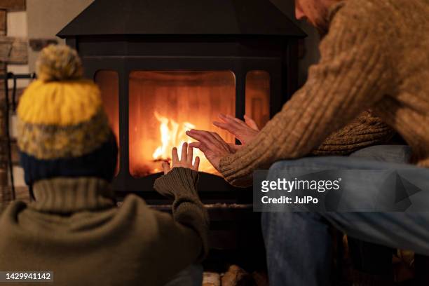 father and son warming hands by a fireplace - hand back lit stock pictures, royalty-free photos & images