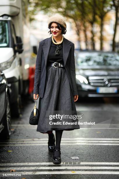 Guest wears a beige fluffy hat, a black t-shirt, black sunglasses, a beige gold large pearls necklace, a gold long necklace, a black striped print...