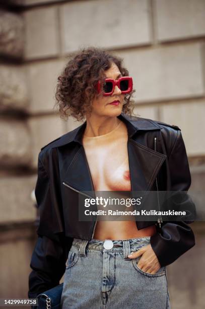 Renia Jaz wearing a black leather cropped jacket, a white and beige body print pattern top, a blue denim long ground touching maxi skirt, a blue...