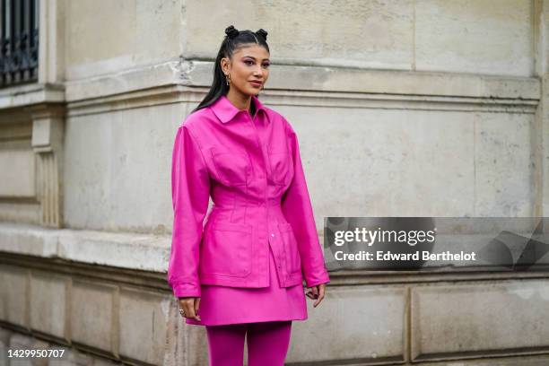 Guest wears gold logo earrings from Valentino, neon pink belted jacket, a neon pink short skirt, neon pink tights, outside Valentino, during Paris...