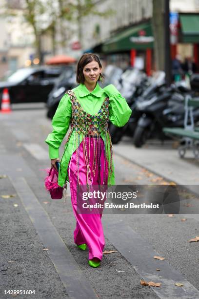 Guest wears gold and green pendant earrings, a neon green long shirt, a brown / yellow / blue / burgundy braided mesh / fishnet V-neck fringed...