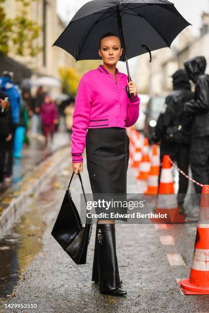 Guest wears a black umbrella, a silver large chain necklace, a neon pink felt bomber coat from Givenchy, a black shiny leather large shoulder bag...