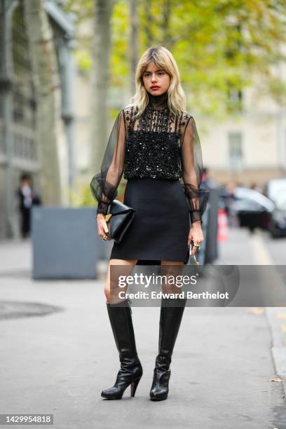 Guest wears a black tulle with embroidered sequined turtleneck / puffy sleeves with embroidered sequined blouse, a black short skirt, a black shiny...