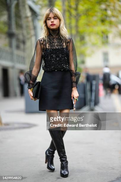 Guest wears a black tulle with embroidered sequined turtleneck / puffy sleeves with embroidered sequined blouse, a black short skirt, a black shiny...