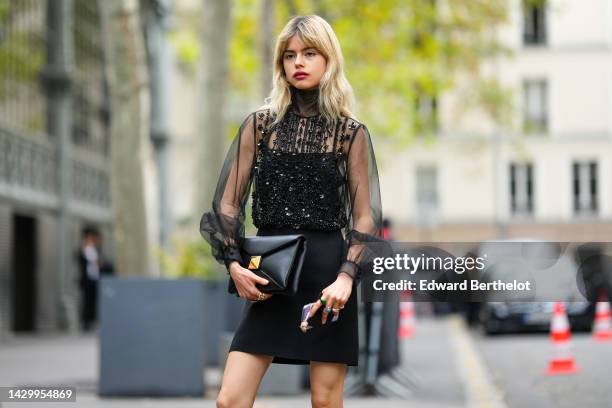 Guest wears a black tulle with embroidered sequined turtleneck / puffy sleeves with embroidered sequined blouse, a black short skirt, a black shiny...