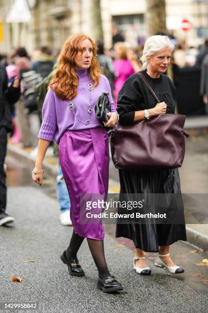 Guest wears a pale purple wool turtleneck pullover, a silver long pendant necklace, a black shiny leather clutch, gold rings, a dark purple shiny...