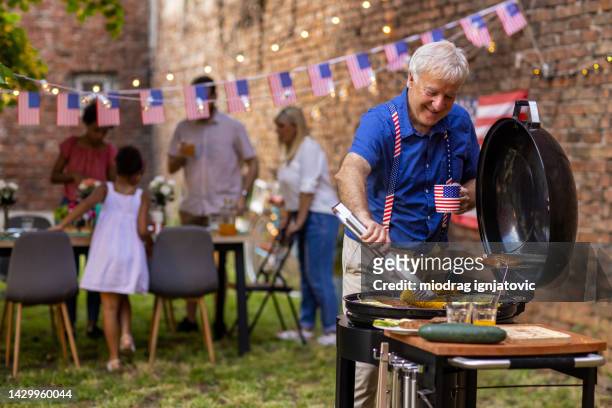 senior man preparing barbeque for american national holiday in a backyard - backyard grilling stockfoto's en -beelden
