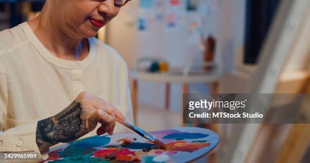 close-up happy asian senior elderly woman, older people, mature lady holding palette color use brush mixing colour create artwork on canvas workshop at night. - adult coloring stock pictures, royalty-free photos & images