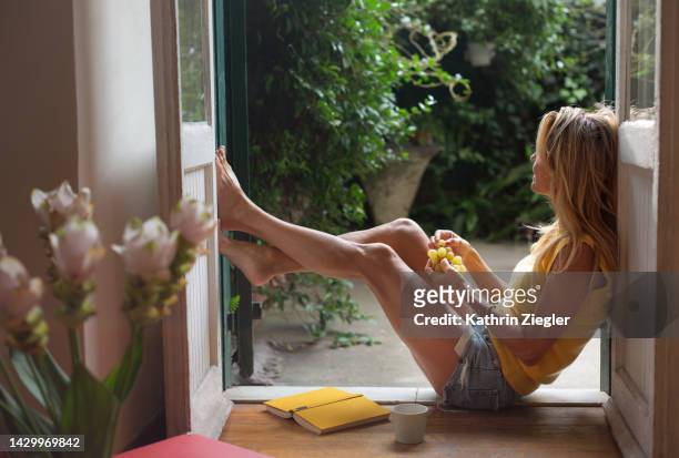 woman leaning on doorway, eating grapes and enjoying the late summer sun - blonde long legs 個照片及圖片檔