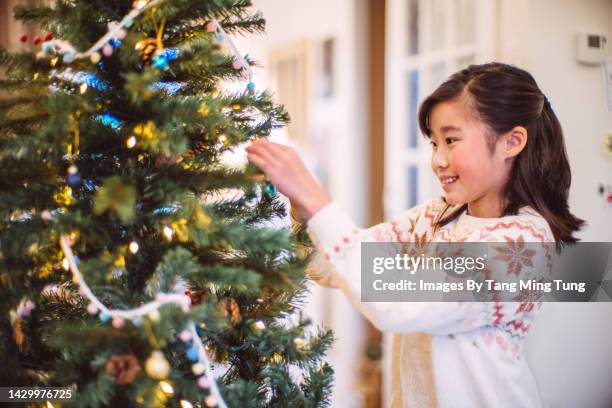 lovely cheerful girl decorating christmas tree at home - children only stock pictures, royalty-free photos & images