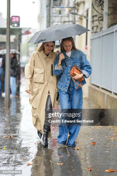 Guest wears a beige long coat, black shiny leather pointed / heels knees boots / waders , a guest wears glasses, a white t-shirt, a blue faded denim...