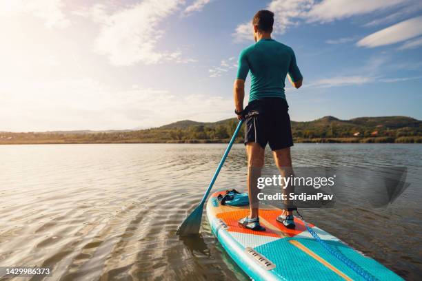 unrecognizable man, paddleboarding with standup paddleboard on a lake - sup stock pictures, royalty-free photos & images