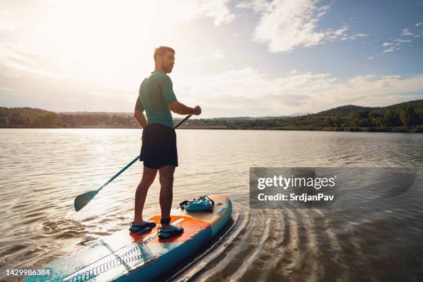 young man, paddleboarding with standup paddleboard on a lake - sup stockfoto's en -beelden