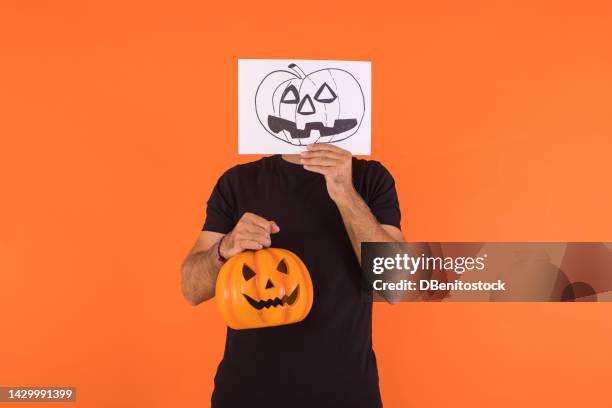 man covering his face with a paper on which a halloween jack o lantern pumpkin is painted, holding a pumpkin, on an orange background. concept of celebration, day of the dead and carnival. - cover monster face bildbanksfoton och bilder