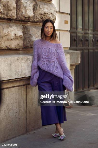 Aimee Song wearing dark purple pants, light pale purple Loewe sweater, beige Loewe bag, and light purple high heels outside Loewe during Paris...