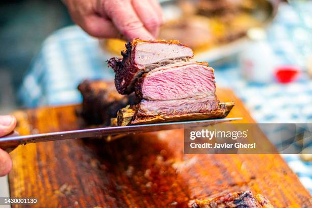 grilled meat and hands cutting with a blade ("asado" - traditional argentine food) - carne asada fotografías e imágenes de stock