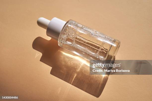 a bottle of serum on a beige background in the rays of the sun close-up with a pipette - facial cleanser stockfoto's en -beelden